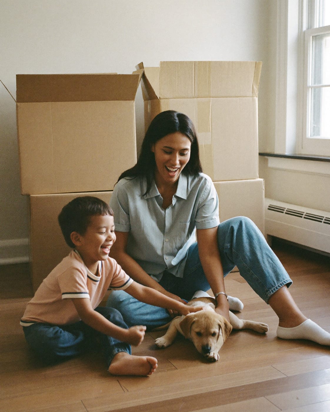 A mother and her young son on moving day, playing with their puppy among moving boxes